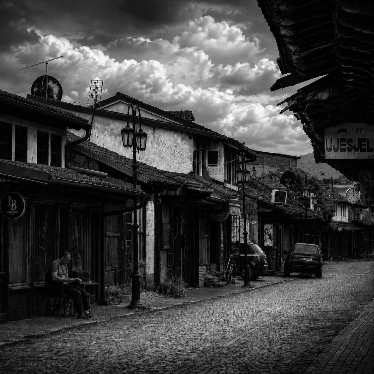 A bazaar lane of timber-fronted shops, a man resting outside one under a dramatic sky.